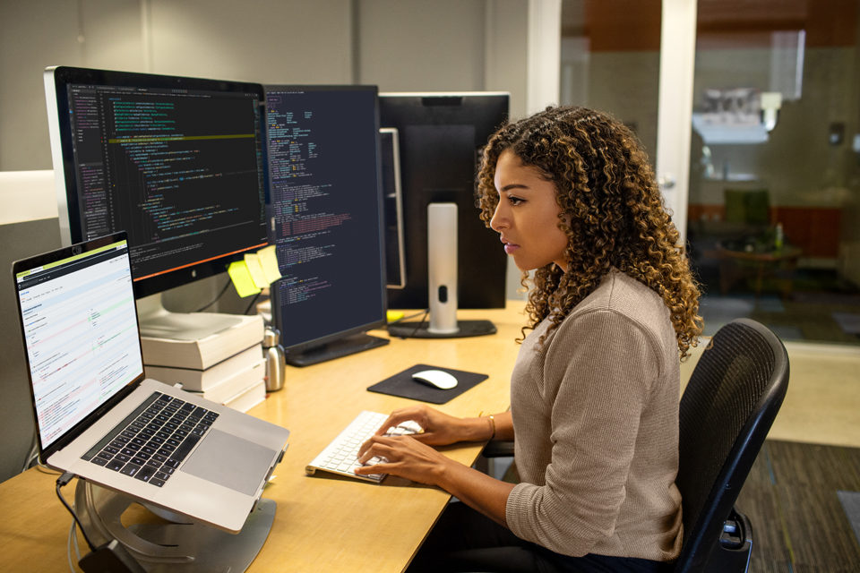 Eine Entwicklerin, die am Büroarbeitsplatz eines Unternehmens arbeitet. Sie hat ihren Arbeitsbereich mit einem Multi-Monitor-Setup angepasst.