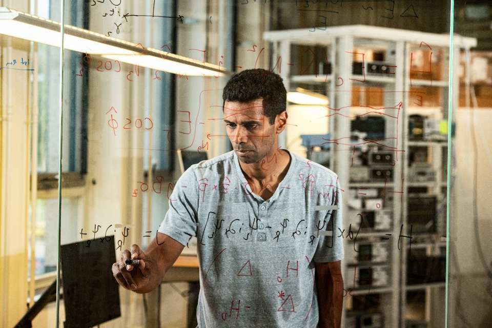 Mann schreibt Zahlen auf eine Glaswand und führt Berechnungen durch