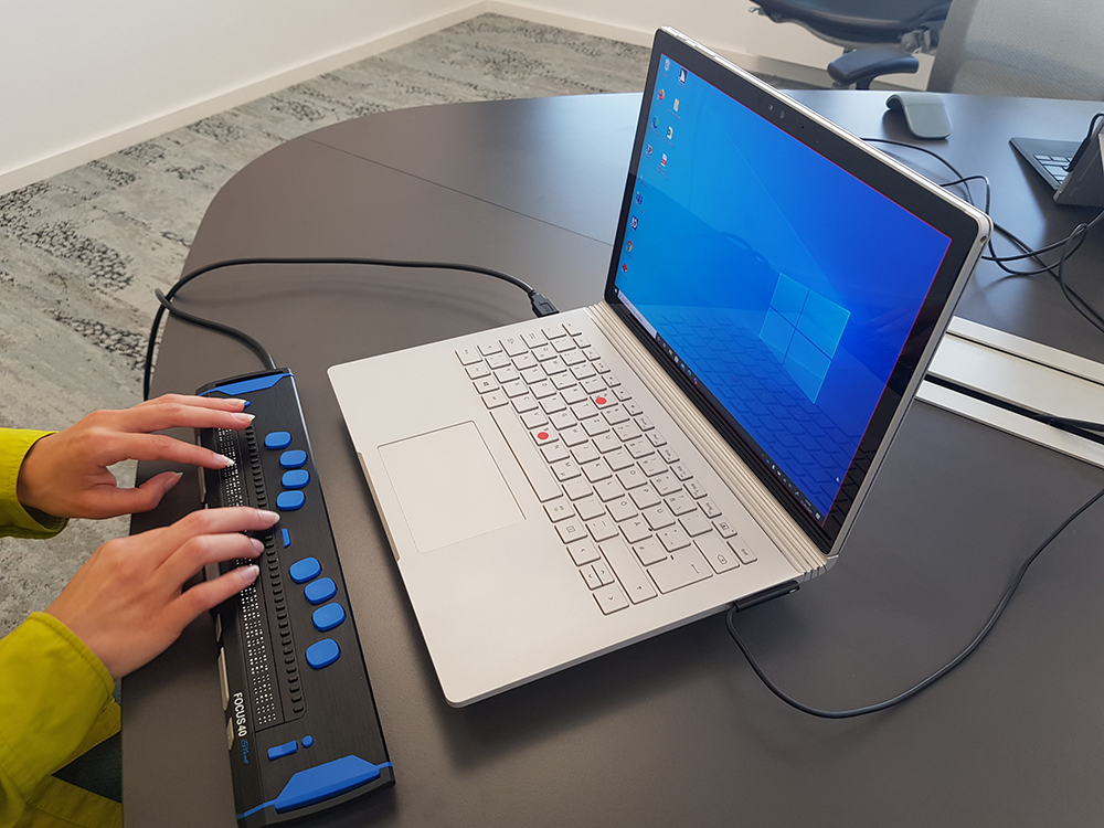 Foto von Laptop und Braille Display mit Händen über Braille Display