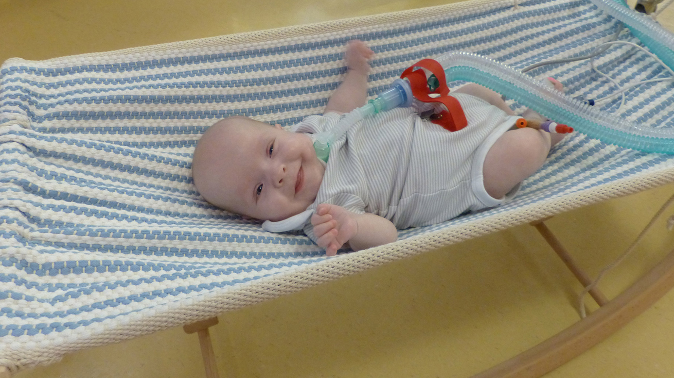 Baby lächelt in die Kamera. Es ist an ein Atemgerät angeschlossen