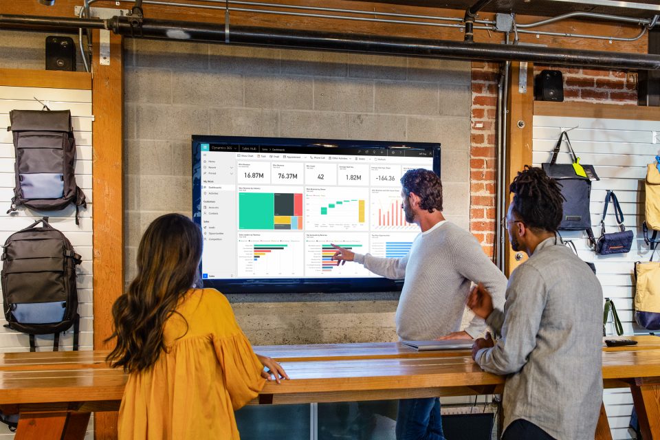 Drei Personen stehen in einer Verkaufsumgebung und evaluieren Daten, die auf einem Bildschirm dargestellt werden.