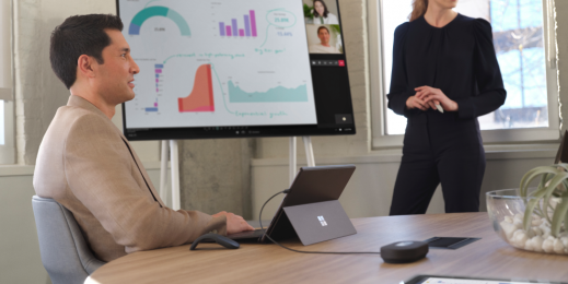 Eine Frau und ein Mann arbeiten in einem hybriden Meetingraum. Hinter ihnen steht ein Surface Hub.