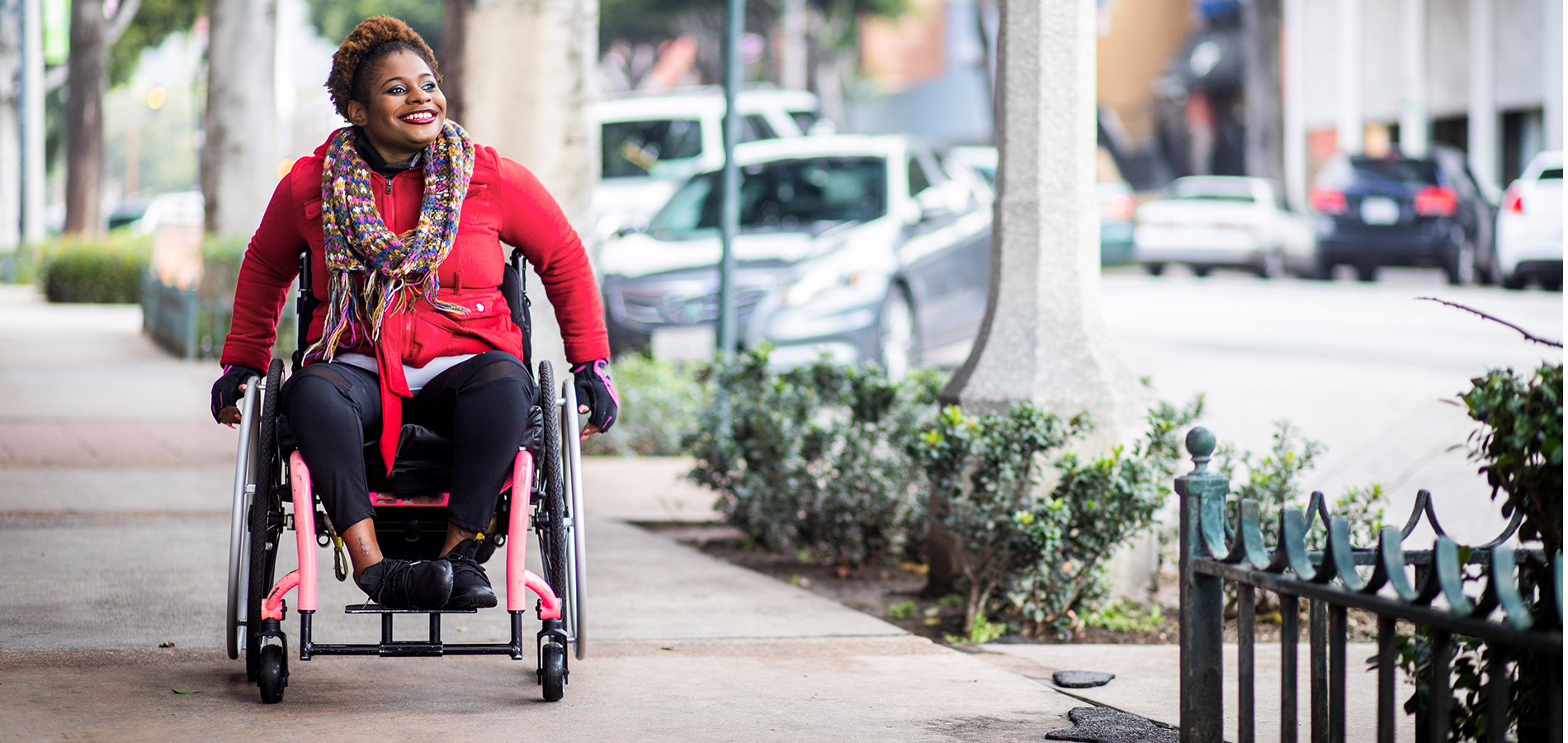 Junge Frau im Rollstuhl unterwegs auf dem Bürgersteig