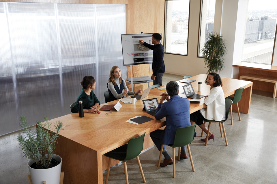Fünf Personen in einem Meetingraum, ein Mann macht Notizen auf Surface Hub