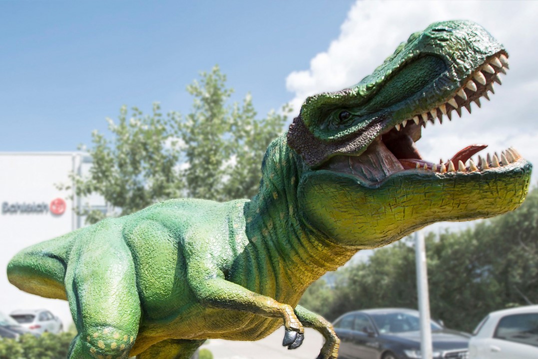 Unternehmensfoto von Schleich mit einem großen Dinosaurier vor dem Gebäude.