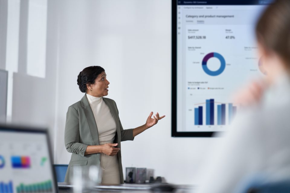 Frau in grauem Blazer präsentiert verschiedene Datenvisualisierung in einem Meeting