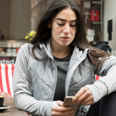 Frau schaut sitzend vor einem Café auf ihr Smartphone