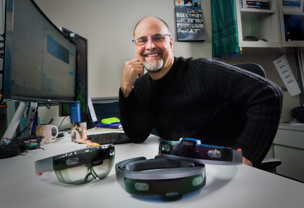 Ed Cutrell, investigador de Microsoft, en su oficina con dispositivos HoloLens frente a él en su escritorio