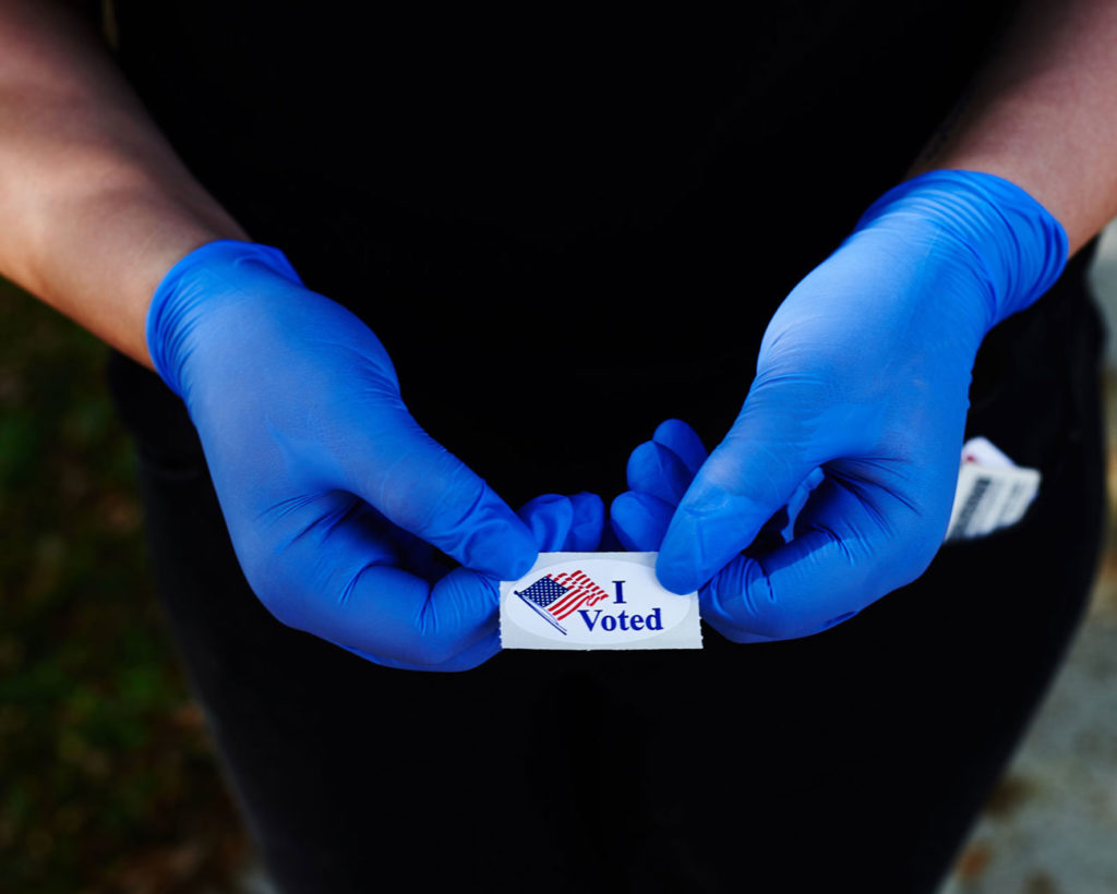 Manos con guantes sostienen un adhesivo de votación