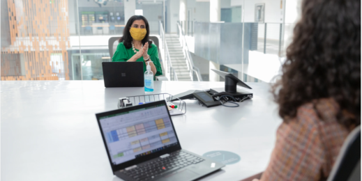 Dos mujeres con cubrebocas en una sala de juntas con laptops