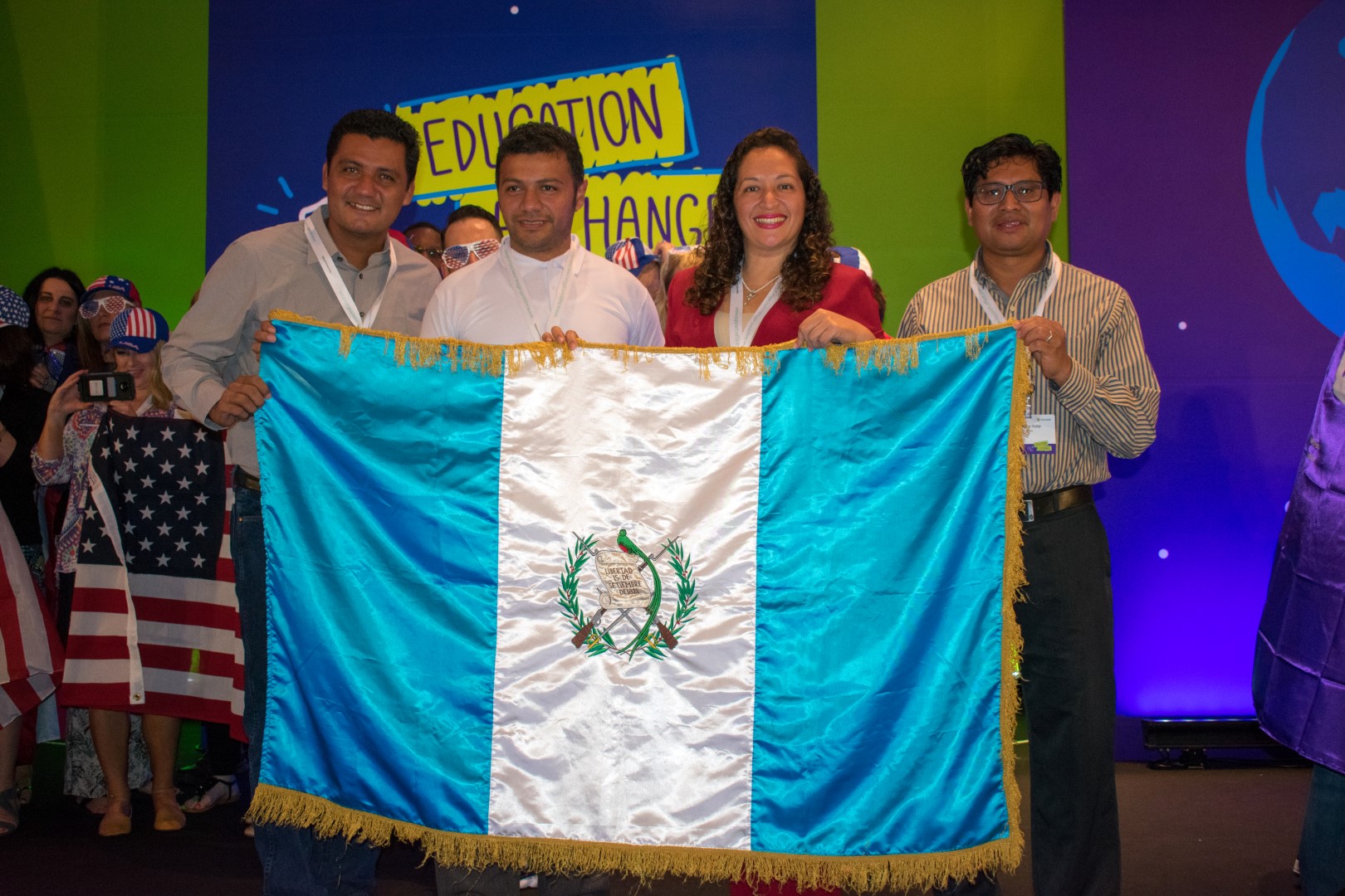 Personas sosteniendo la bandera de Guatemala frente a un letrero de Education Exchange