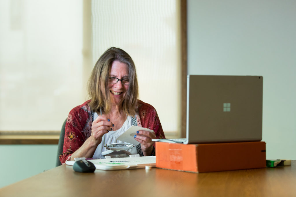Una mujer trabaja con cuentas mientras está sentada en una mesa frente a una laptop.