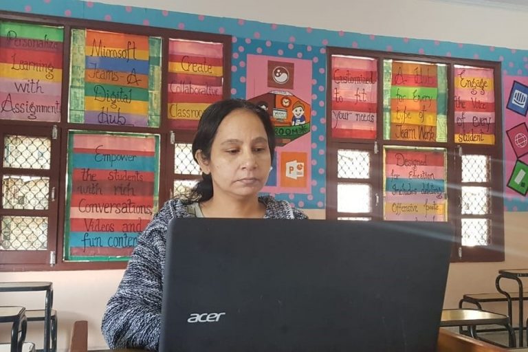 Profesora trabaja en una laptop en un aula con un fondo colorido