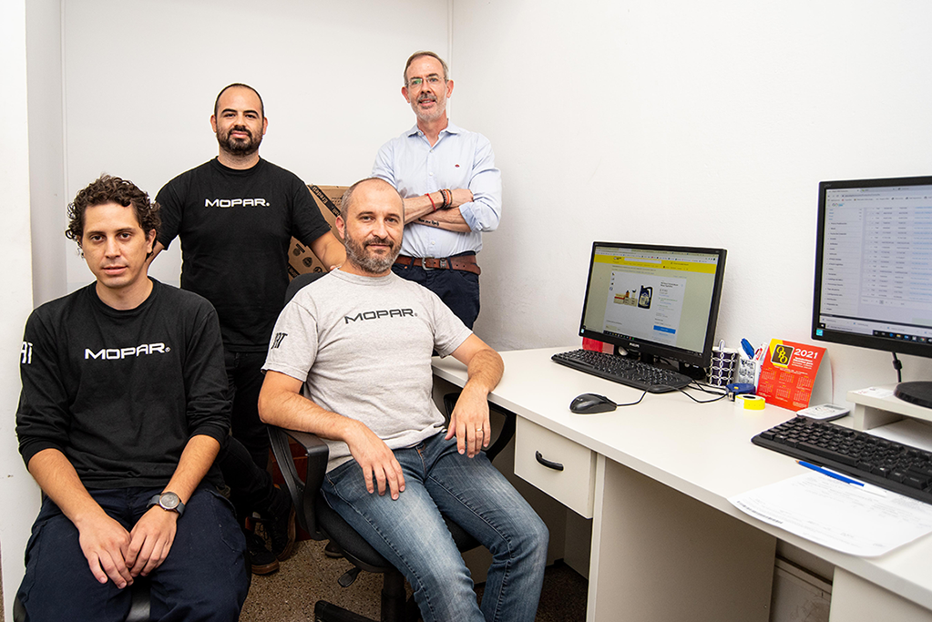 4 hombres posan para la foto junto a un escritorio con laptops