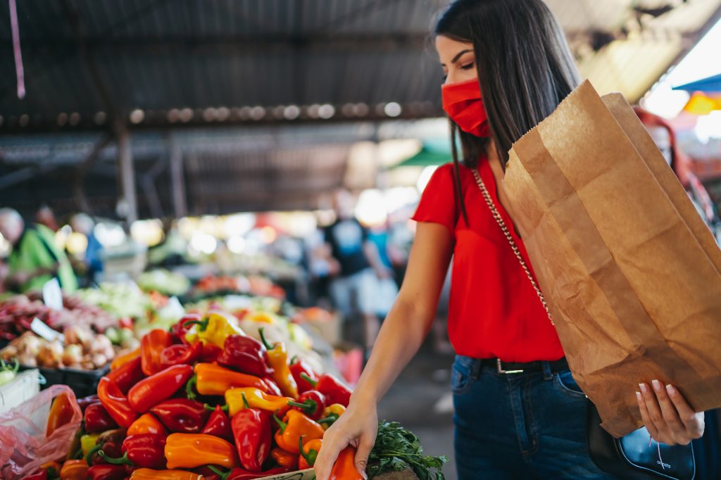 Una mujer con cubrebocas en un mercado de alimentos con una bolsa