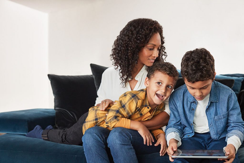 Una madre con sus dos hijos sentados en un sofá juegan con una laptop