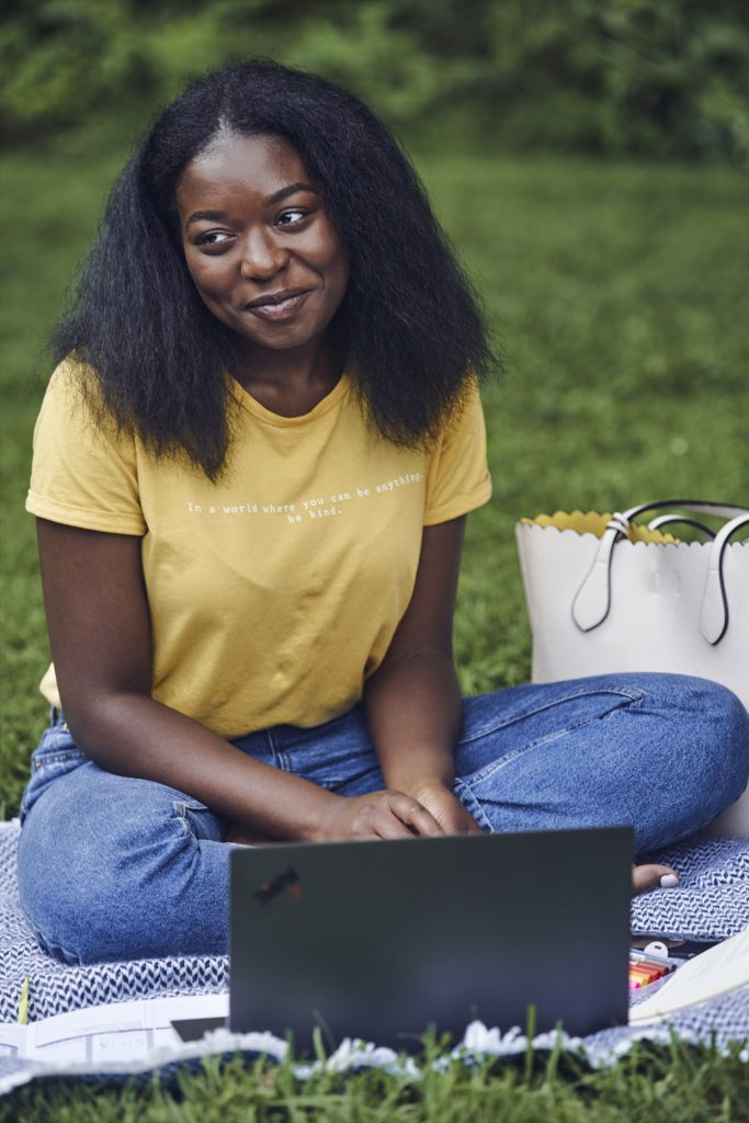 Mujer sentada frente a una laptop en un campo con hierba