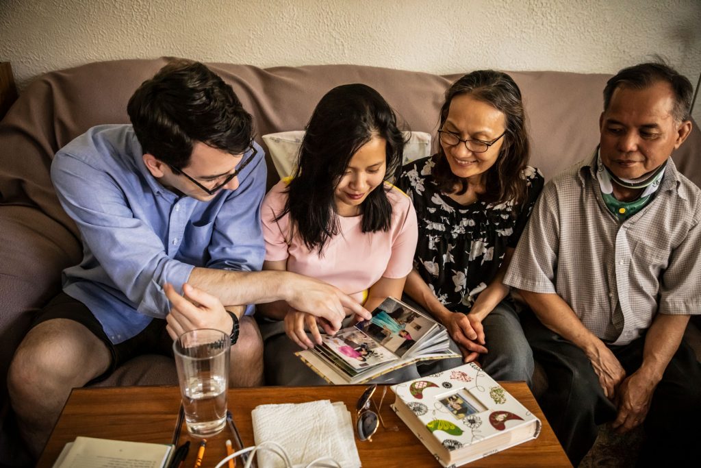 Houng Haley sentada en un sofá con su esposo y sus padres, miran juntos fotos en un álbum de recortes.