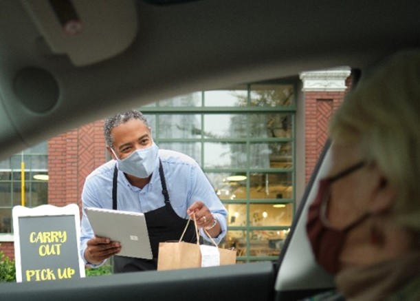 Una persona en un auto, con cubrebocas, recibe un paquete de comida