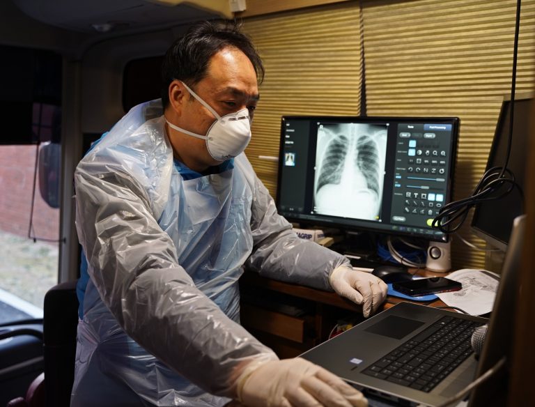 Un hombre con mascarilla en un teclado de computadora con una radiografía en una pantalla