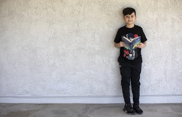 niño está apoyado contra una pared, mientras sostiene un libro
