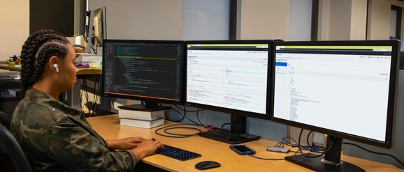 Una mujer sentada en un escritorio frente a tres monitores