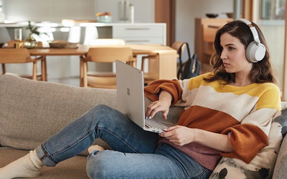 Una mujer en un sofá con una laptop en las piernas con audífonos
