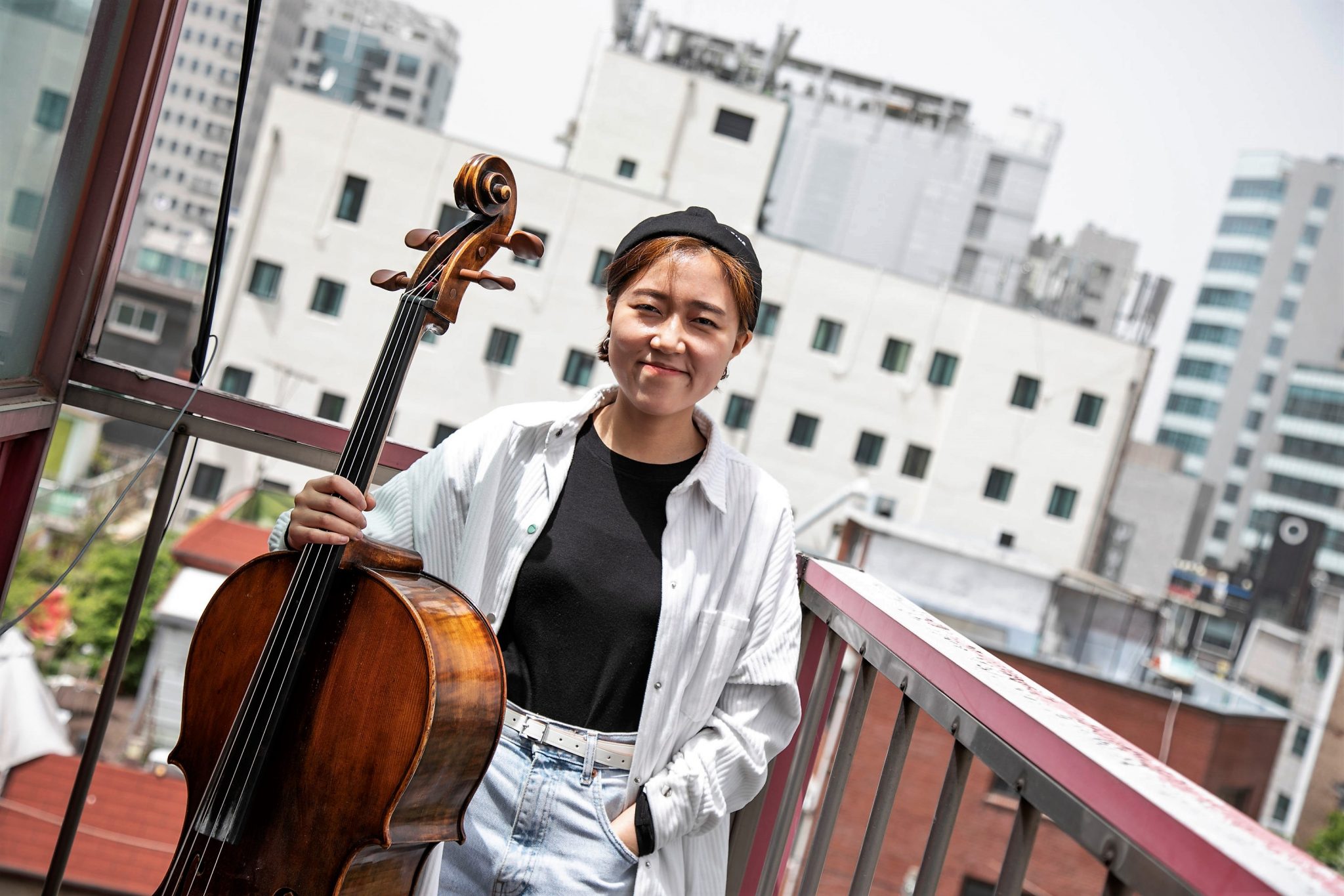 Una mujer sonriente de pie con un violonchelo con un horizonte de la ciudad de fondo