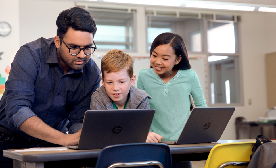 Un profesor trabaja con dos niños con sus laptops