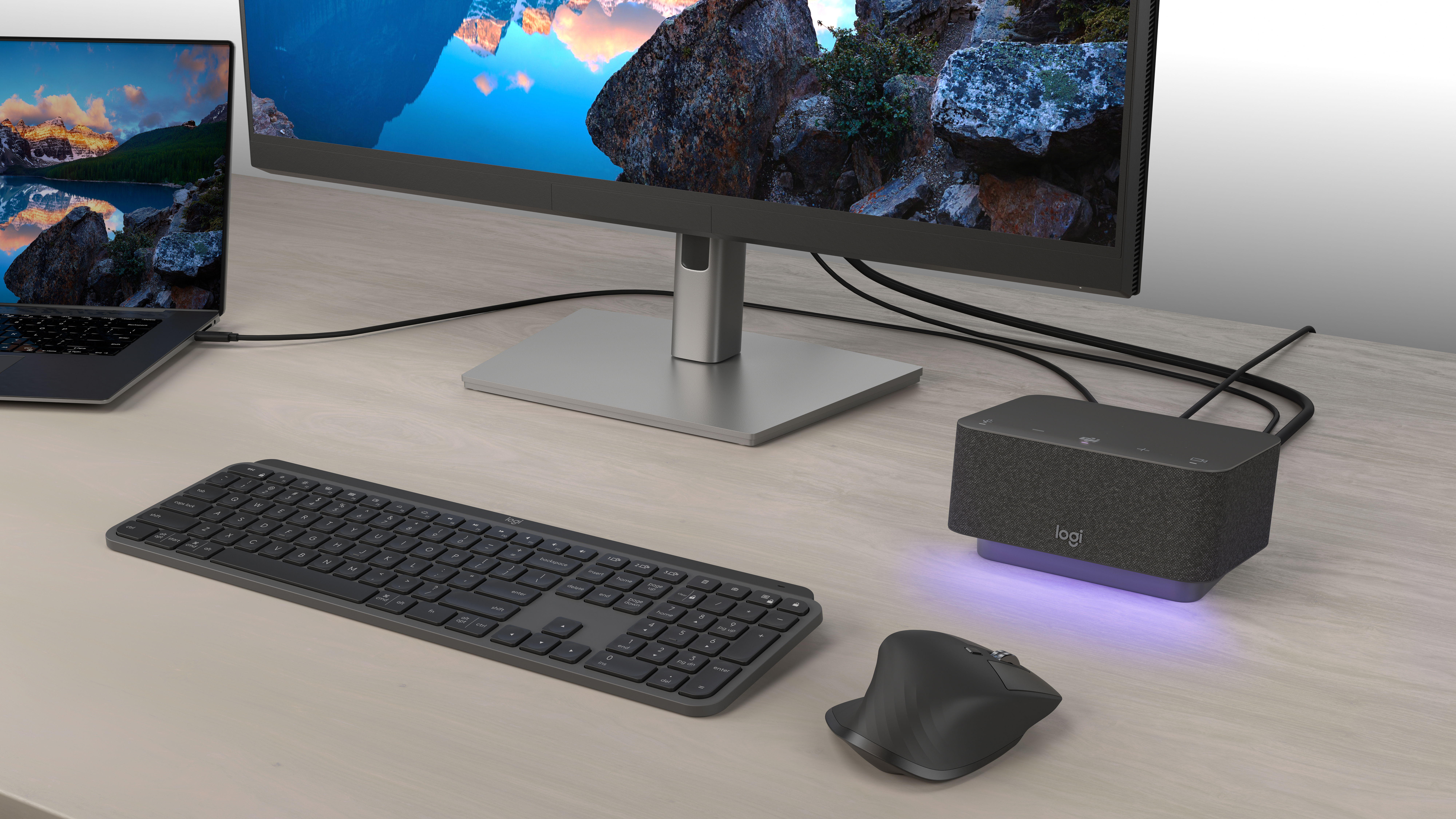 Altavoz integrado en la caja rectangular negra con luz morada tenue junto a la portátil, el monitor, el teclado inalámbrico y el ratón.