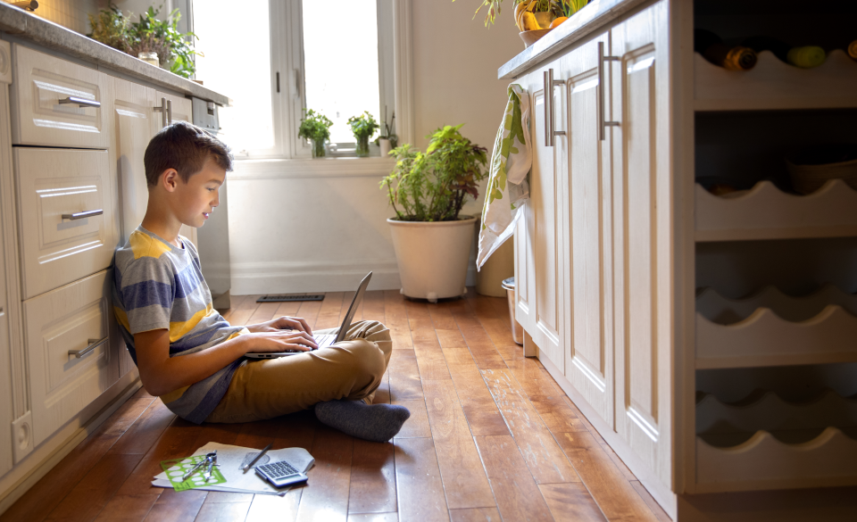 Un niño sentado en el piso de una casa con una laptop en sus piernas