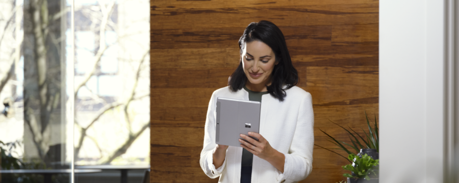 Mujer adulta sostiene una Surface Go 3 de platino en modo tableta mientras está en una oficina.