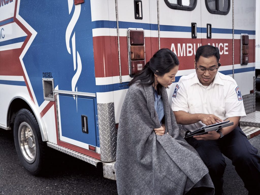 Una mujer se sienta en el parachoques de una ambulancia con un EMT