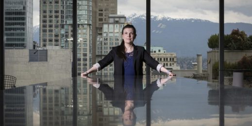 Katie Peters, desarrolladora de personal de TELUS, sentada en una mesa de conferencias en la sede de la empresa, el cielo y las montañas se reflejan en la superficie brillante de la mesa.