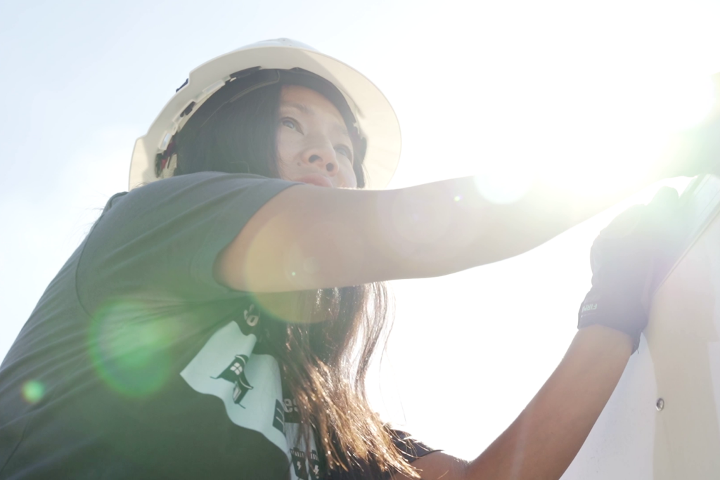 Imagen de una mujer joven que usa un casco y trabaja en un remolque que funciona con energía solar en el lugar de un desastre.