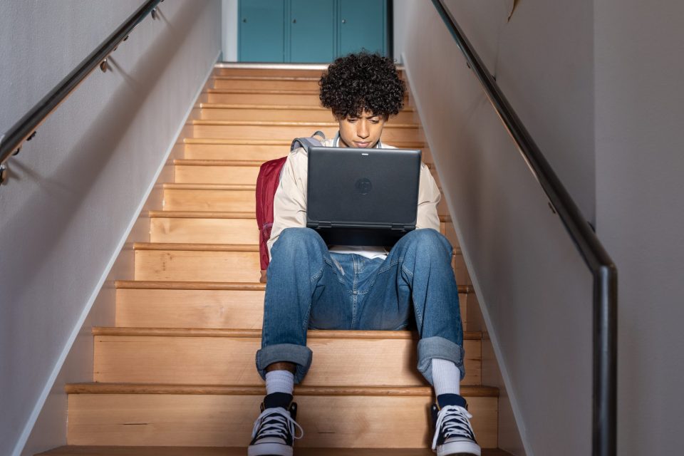 Una persona joven sentada en unas escaleras usa su laptop