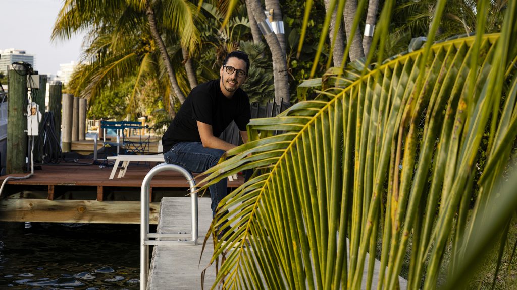 Rafael Lourenco, de la fintech ClearSale, con anteojos y playera negra sentado al borde de una alberca junto a palmeras