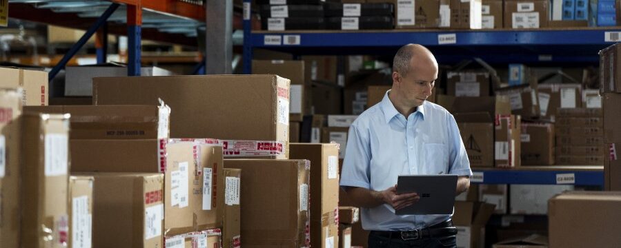 Un trabajador de primera línea en un almacén de la cadena de suministro usa un dispositivo Surface como tableta para tomar notas.