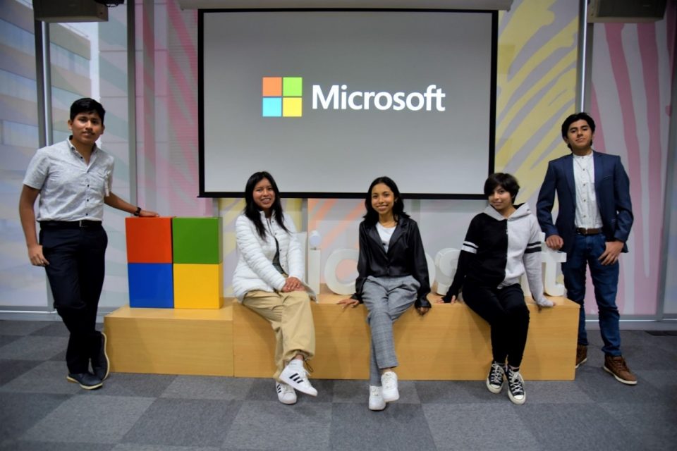 Cinco jóvenes posan frente al logo de Microsoft