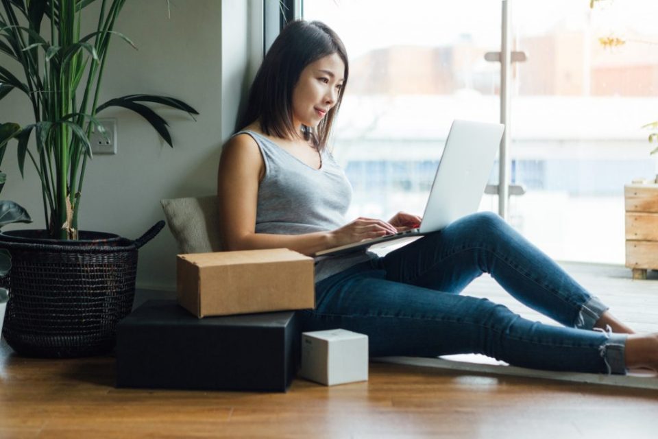Mujer en casa trabaja en una computadora portátil con paquetes a su lado
