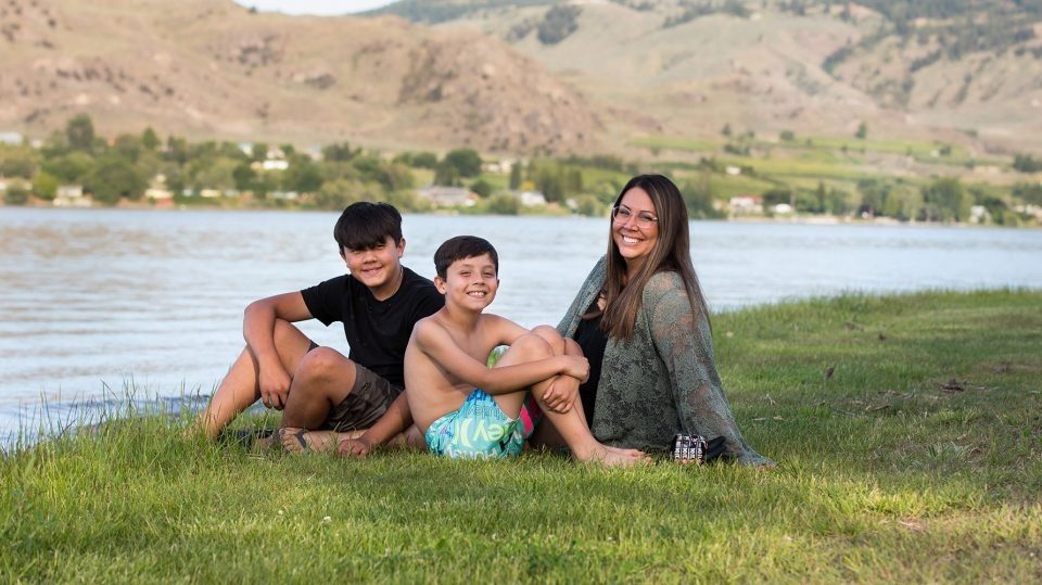 mãe e dois filhos sentados na grama sorrindo