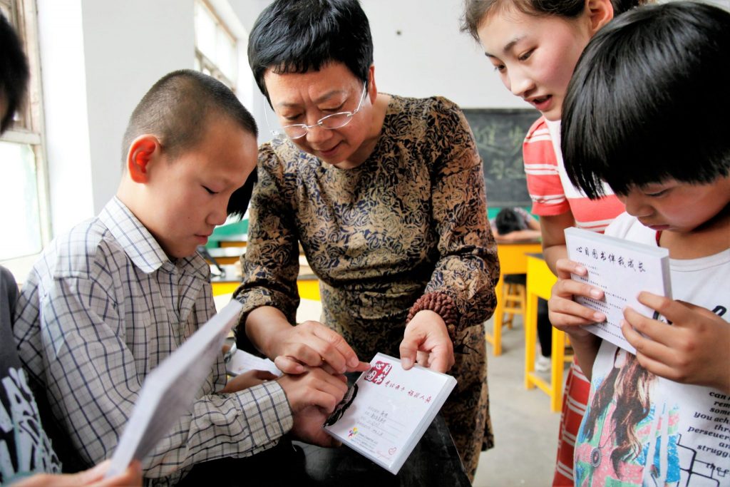 mulher de cabelo curto e óculos auxiliando crianãs com deficiência visual a ler