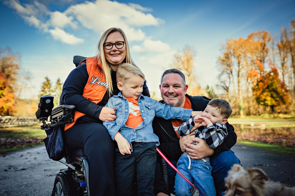 mulher sorrindo sentada em cadeira de rodas com uma criança no colo e homem sentado do lado com criança nos braços