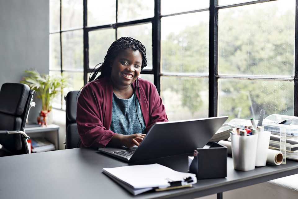 Retrato de uma empresária sorridente com deficiência visual trabalhando em laptop no local de trabalho moderno.