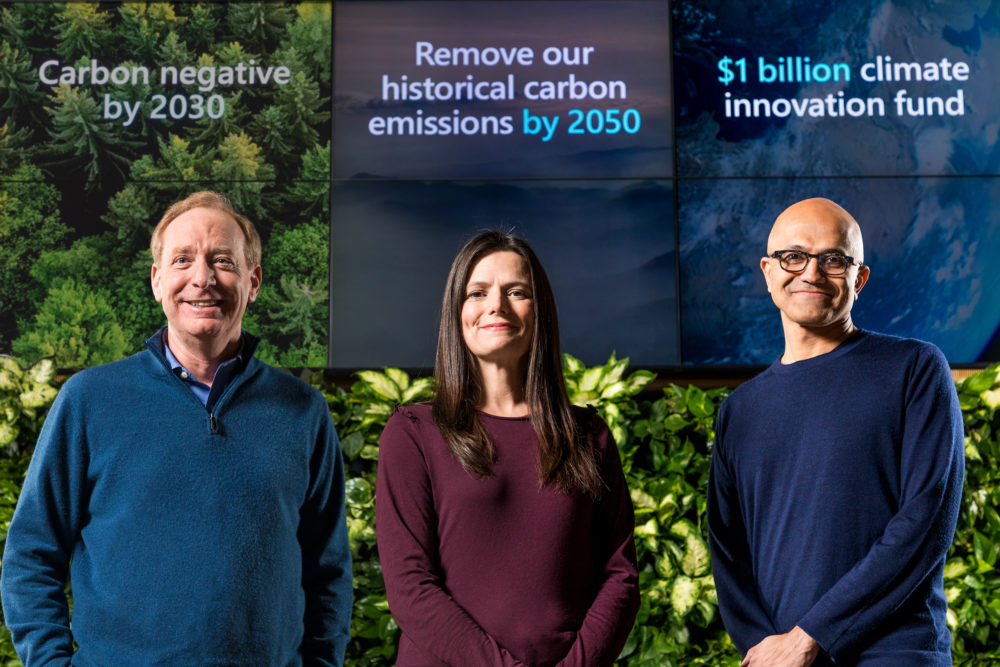 Brad Smith, Amy Hood, Satya Nadella standing in front of a screen