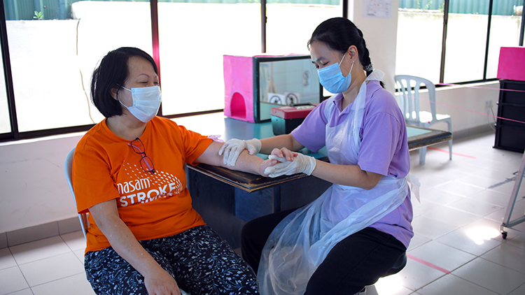 A health professional tends to a patient. Both are seated and are wearing face masks.