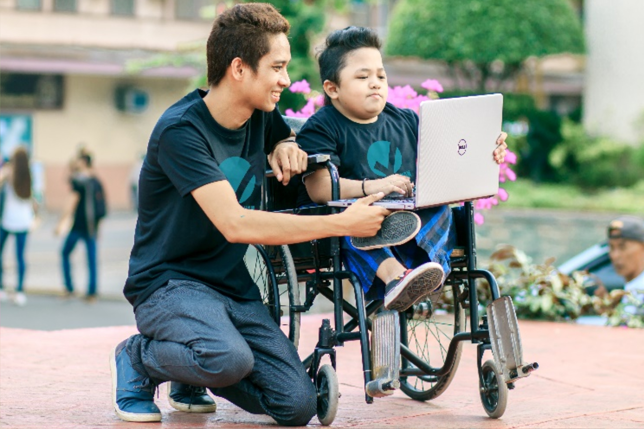 A man kneels and another man sits in a wheelchair
