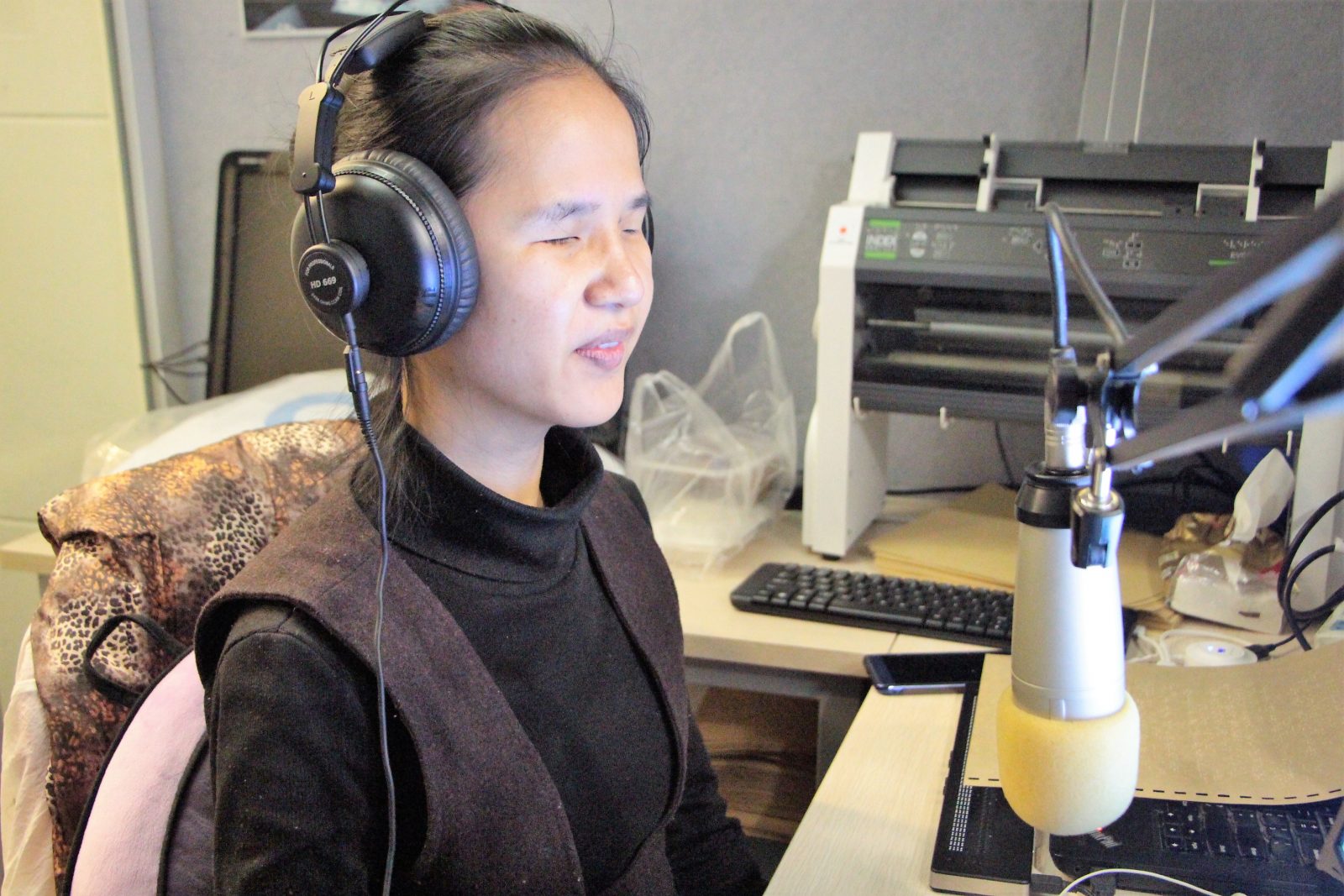 A woman wearing headphones and taliing into a microphone.