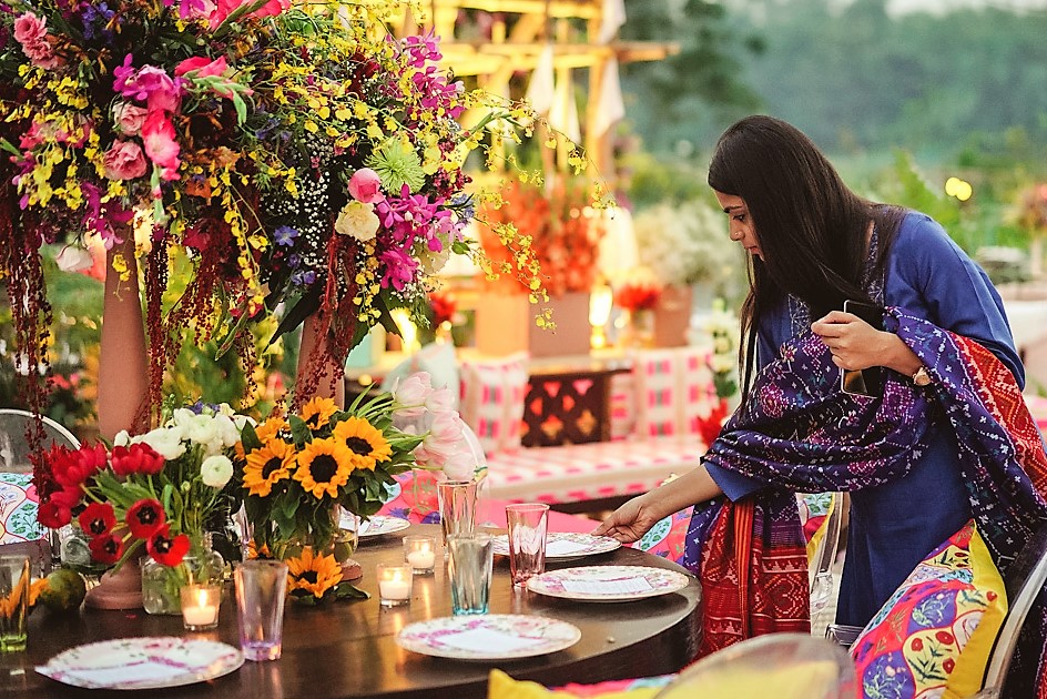 A woman lays a table that also has flowers.