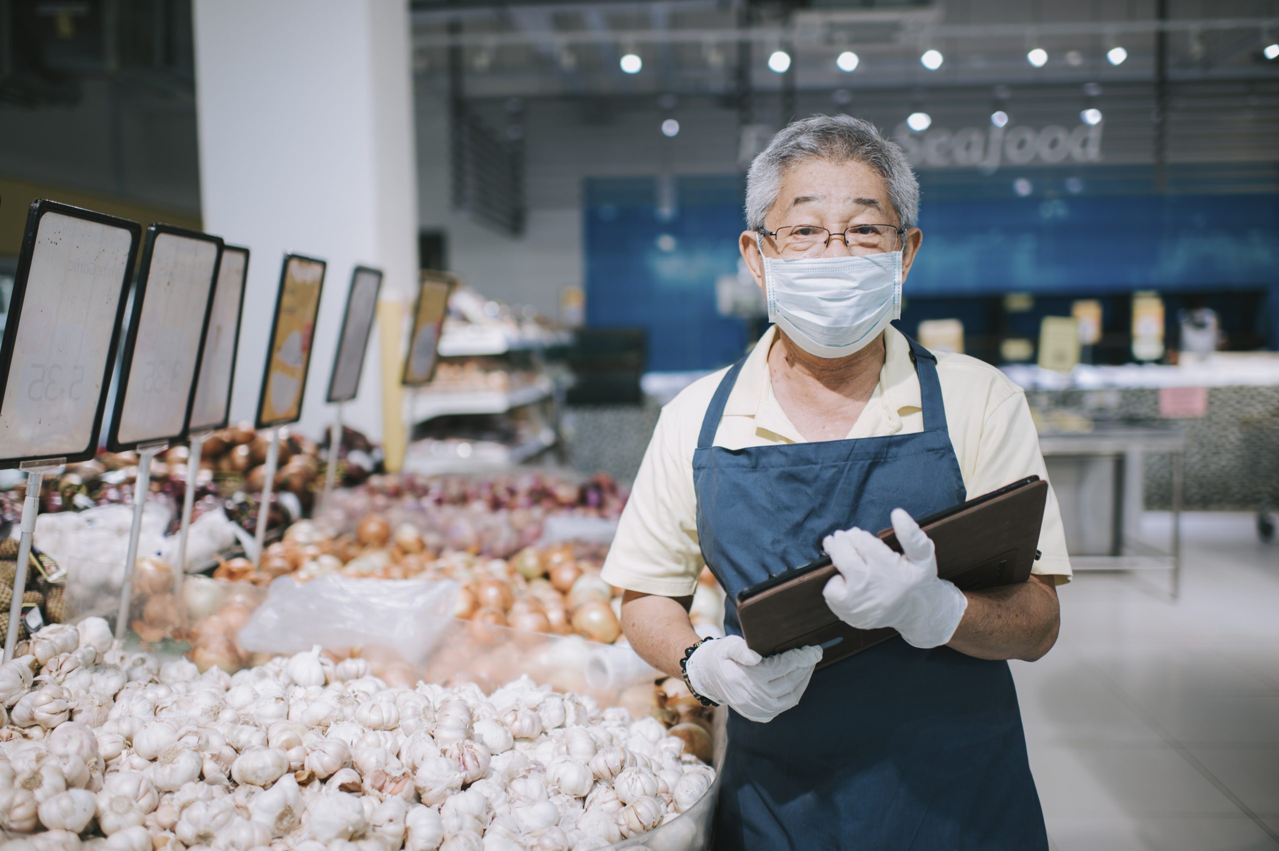 An asian chinese senior man supermarket shopkeeper retail assistant with face mask